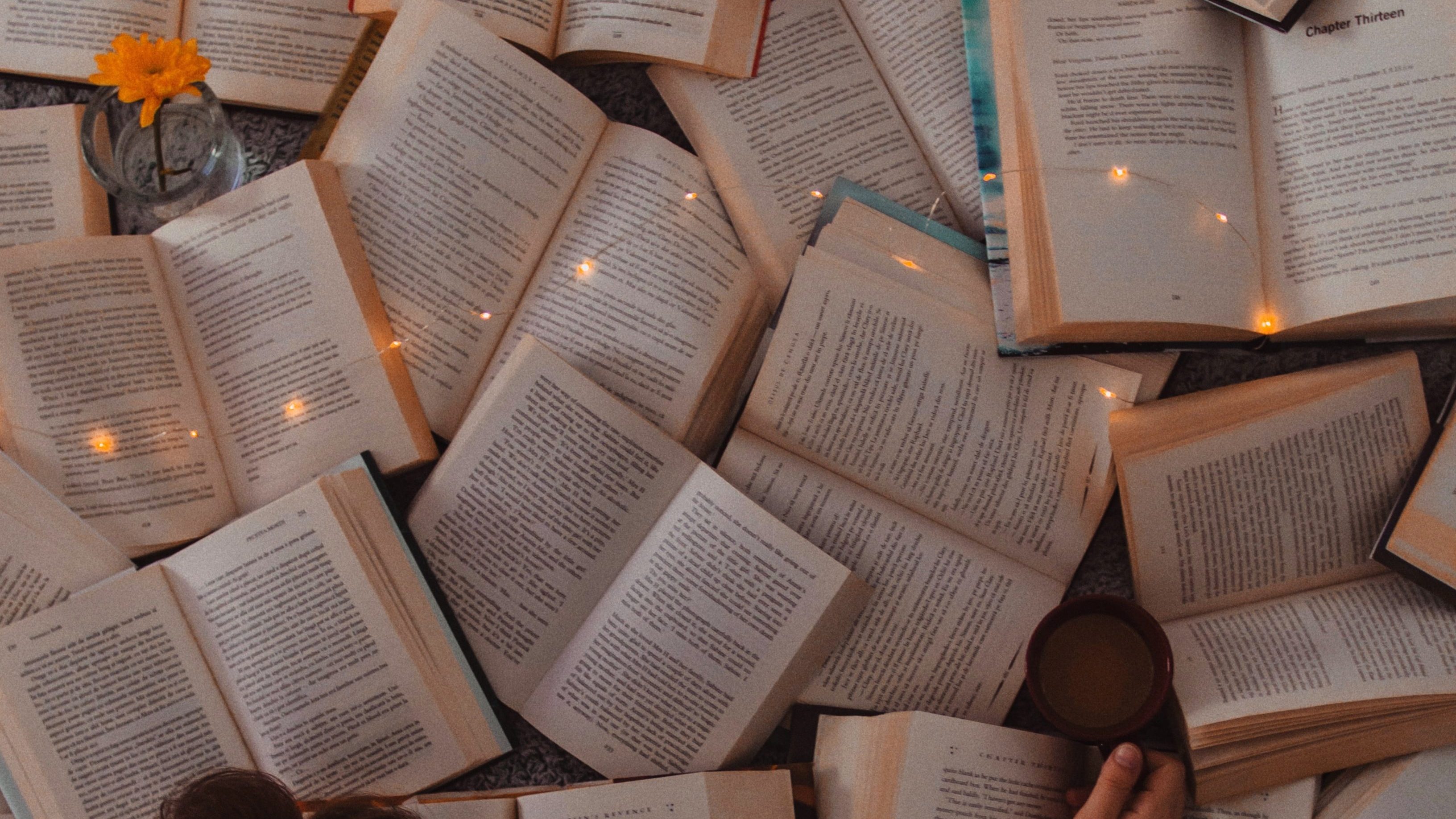 Imagem com vários livros abertos em páginas de texto sobre uma mesa com luzes sobre alguns deles. 
