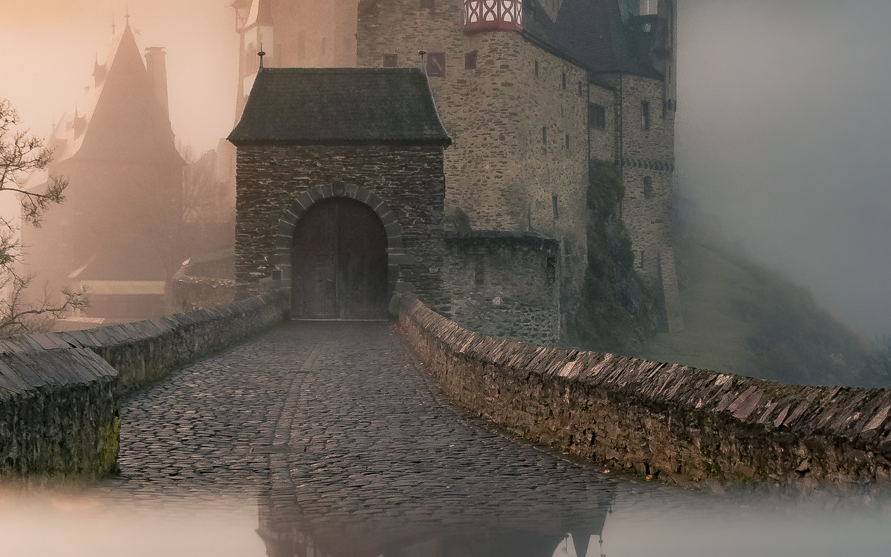 Imagem de um castelo antigo em neblina, com reflexo abaixo, remetendo a fantasia medieval. 